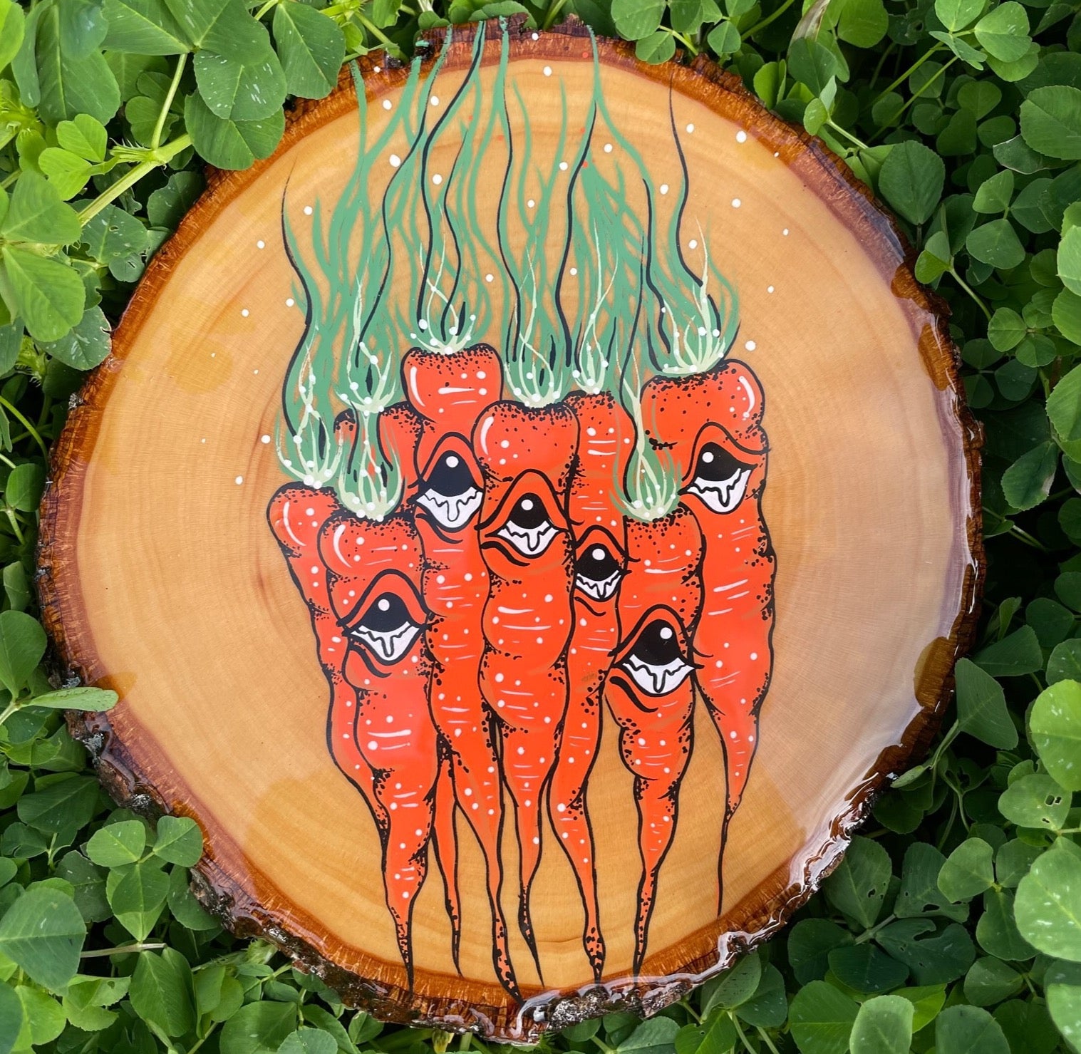A photo of Louisiana artist, Tristen Rolling's original acrylic painting of a bunch of carrots on a round slice of oak wood. The painting is coated in a layer of epoxy resin and reflects Tristen's love for Louisiana farmers markets.  