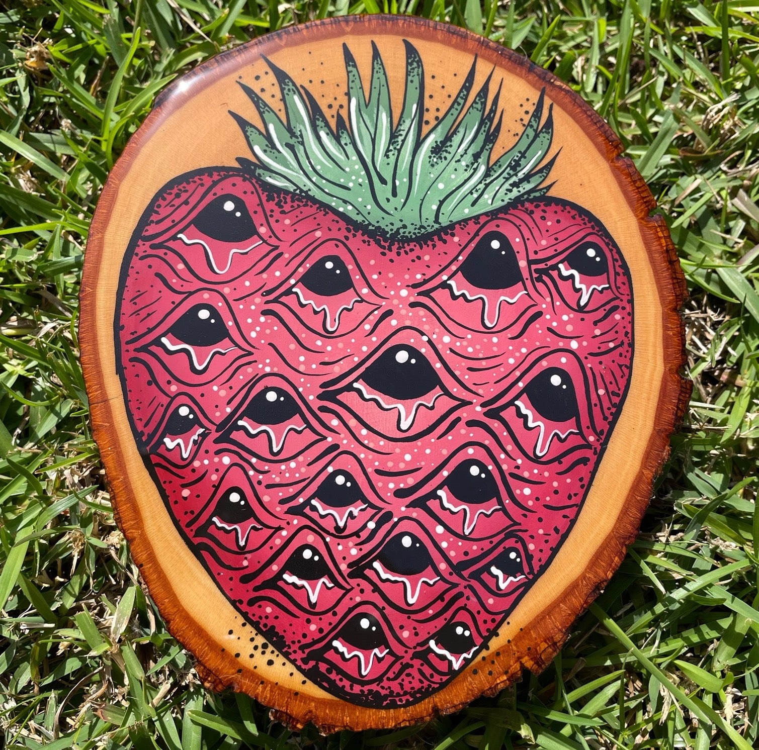 A photo of Louisiana artist, Tristen Rolling's original acrylic painting of a Louisiana strawberry on a round slice of oak wood. The painting is coated in a layer of epoxy resin and reflects Tristen's love for Louisiana farmers markets.  